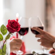 Toasting two wine glasses next to a red rose