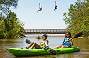 two girls on a green kayak with two people ziplining in the background